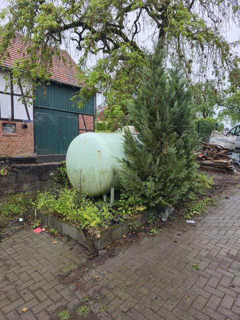 Bepflanzter Bereich am Gastank vor Fachwerkhaus